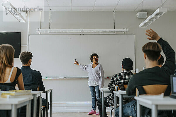 Reife Lehrerin zeigt auf Whiteboard  während sie Schüler im Klassenzimmer unterrichtet