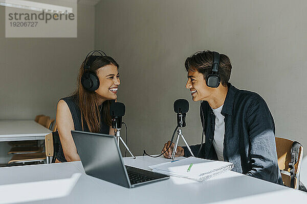 Glückliche männliche und weibliche Schüler schauen sich beim Podcasting im Klassenzimmer an