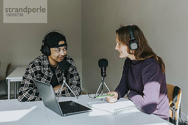 Junge männliche und weibliche Studenten unterhalten sich während des Podcasts im Klassenzimmer