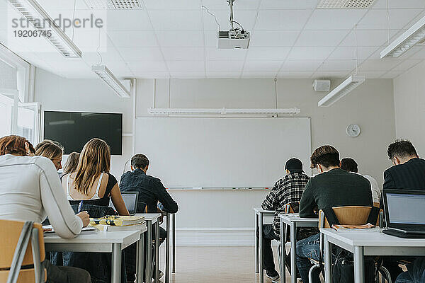 Rückansicht von Schülern  die im Klassenzimmer mit leerem Whiteboard lernen