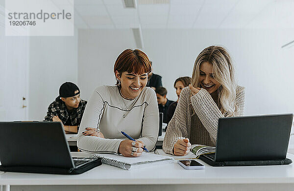 Fröhliche Studentinnen lernen gemeinsam am Schreibtisch im Klassenzimmer