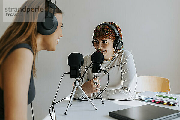 Fröhliche Mädchen im Teenageralter unterhalten sich während des Podcasts am Schreibtisch im Klassenzimmer