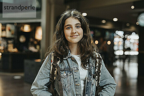 Porträt eines lächelnden Mädchens mit langen Haaren und Jeansjacke am Bahnhof