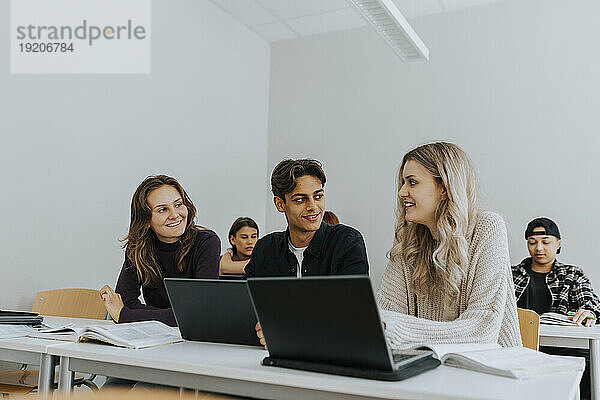 Lächelnde Schüler sitzen am Schreibtisch  während sie gemeinsam im Klassenzimmer lernen