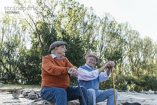 Zwei alte Freunde sitzen auf einem Baumstamm am Flussufer und teilen Erinnerungen