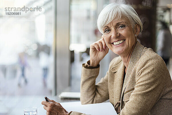 Porträt einer lächelnden älteren Geschäftsfrau mit Notizbuch in einem Café