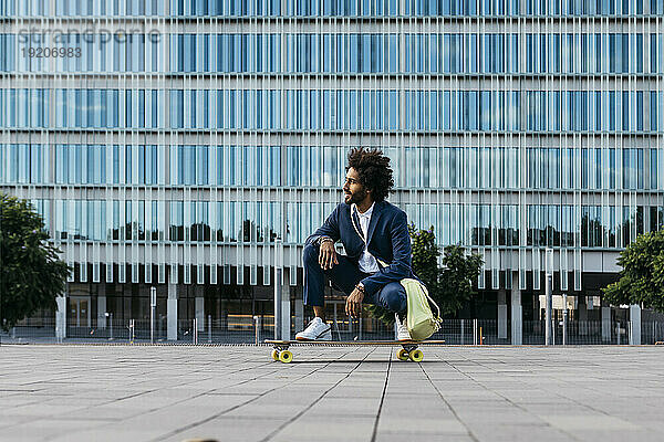 Spanien  Barcelona  ??junger Geschäftsmann kauert auf Skateboard in der Stadt