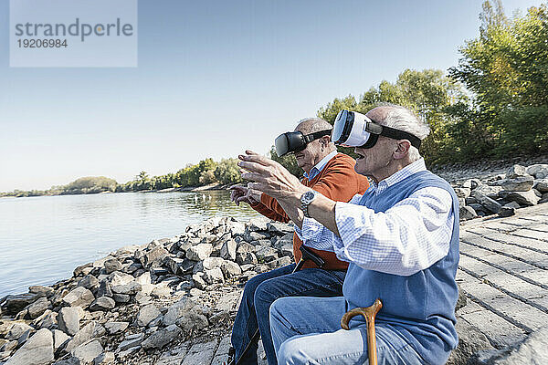 Zwei alte Freunde sitzen am Flussufer und benutzen eine VR-Brille