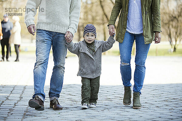 Porträt eines Jungen  der Hand in Hand mit seinen Eltern geht