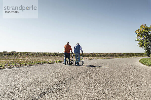 Zwei alte Freunde laufen mit Rollatoren auf einer Landstraße
