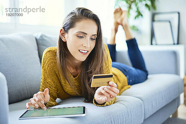 Schöne lächelnde Frau kauft online mit Tablet und Kreditkarte