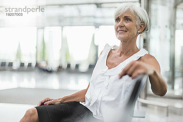 Lächelnde ältere Frau sitzt im Wartebereich und schaut sich um