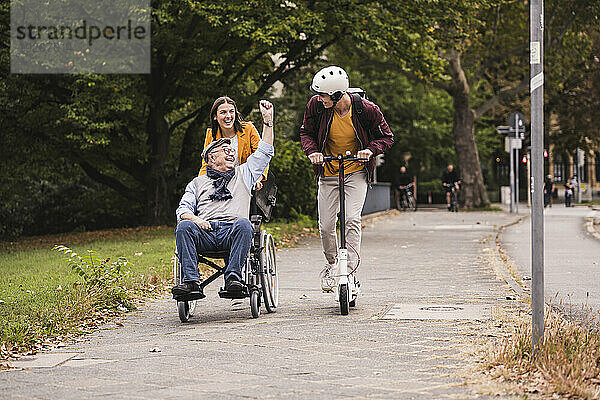 Älterer Mann im Rollstuhl vergnügt sich mit seinen erwachsenen Enkelkindern im Freien