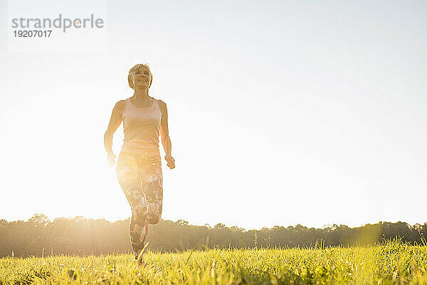 Senior woman running on rural meadow at sunset