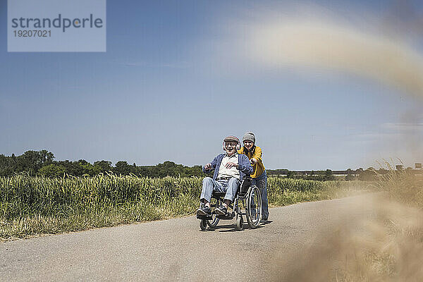 Mädchen schiebt Rollstuhl mit Großvater an sonnigem Tag
