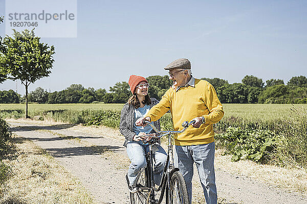 Glücklicher Großvater mit Enkelin  die auf dem Fahrrad auf dem Feld sitzt