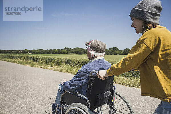 Glückliches Mädchen  das an einem sonnigen Tag mit seinem Großvater den Rollstuhl schiebt