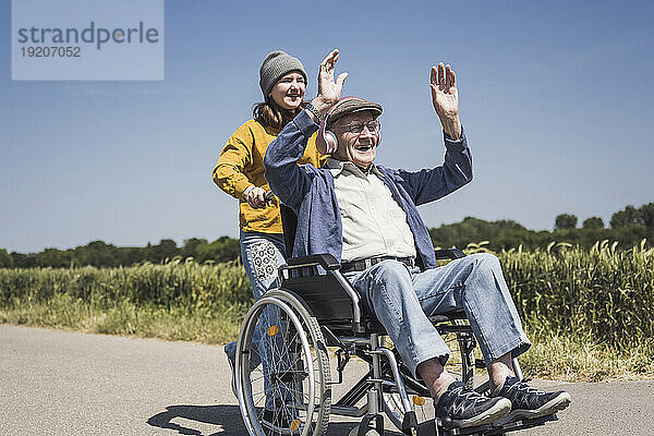 Lächelndes Mädchen mit Großvater  der im Rollstuhl sitzt und Musik hört