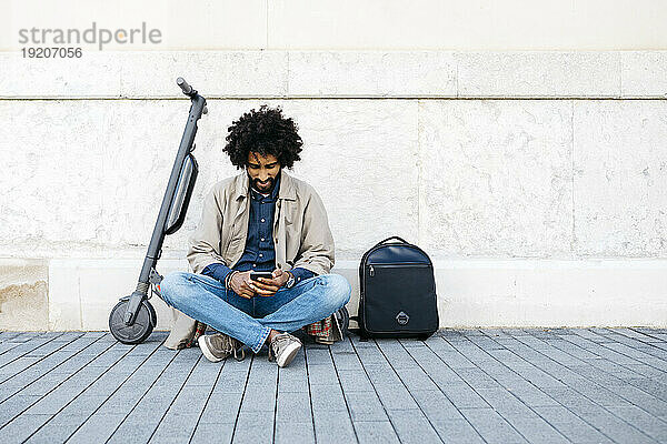 Mann sitzt auf seinem E-Scooter und nutzt sein Mobiltelefon