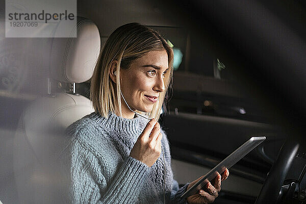 Lächelnde junge Frau mit Tablet und Kopfhörern in einem Auto