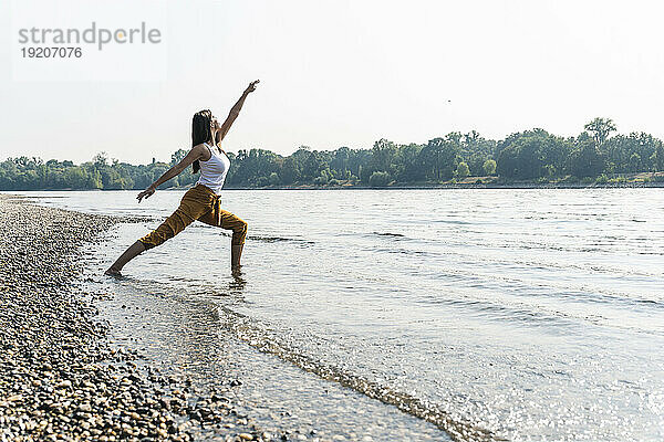 Junge Frau steht im Wasser eines Flusses und praktiziert Yoga