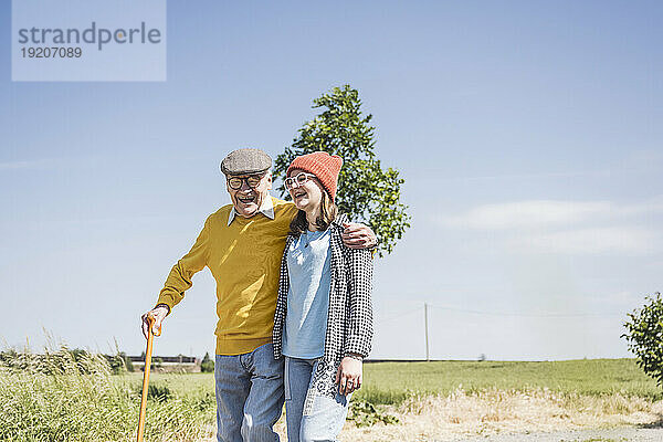Glücklicher älterer Mann  der an einem sonnigen Tag mit seiner Enkelin spaziert