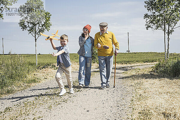Lächelndes Mädchen und Junge  die Spaß mit Großvater haben und auf der Straße spazieren gehen