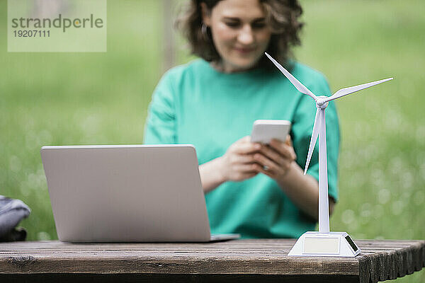 Laptop und Windturbinenmodell im Fokus  im Hintergrund Geschäftsfrau mit Smartphone