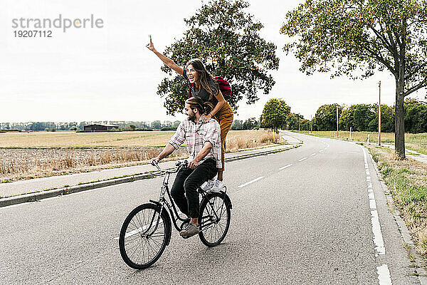Glückliches junges Paar  das zusammen auf einem Fahrrad auf der Landstraße fährt