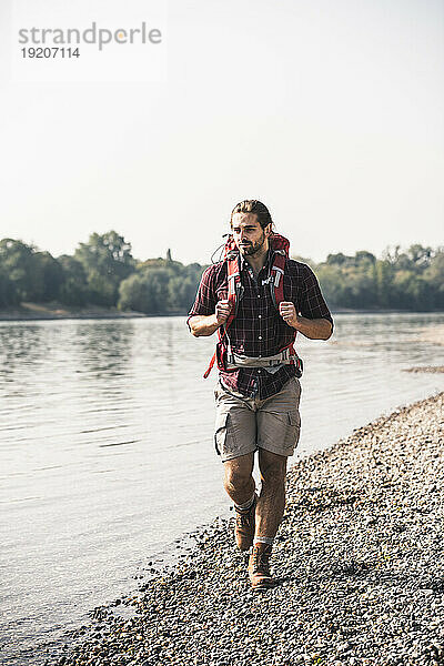 Junger Mann mit Rucksack spaziert am Flussufer