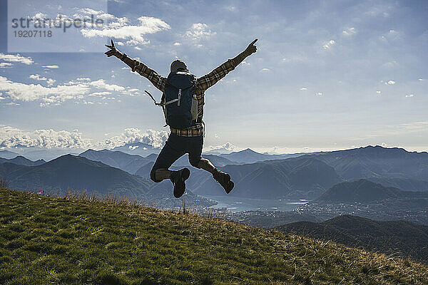 Glücklicher Wanderer springt mit erhobenen Armen auf den Berg
