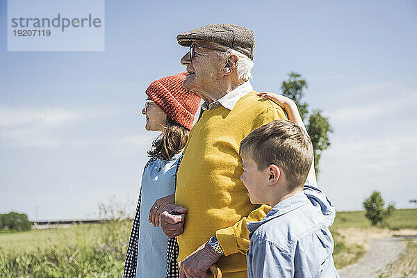 Älterer Mann steht mit Enkelin und Enkel an einem sonnigen Tag