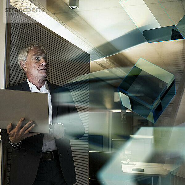 Digitales zusammengesetztes Bild eines nachdenklichen Geschäftsmannes mit Laptop und futuristischen Würfeln im Büro