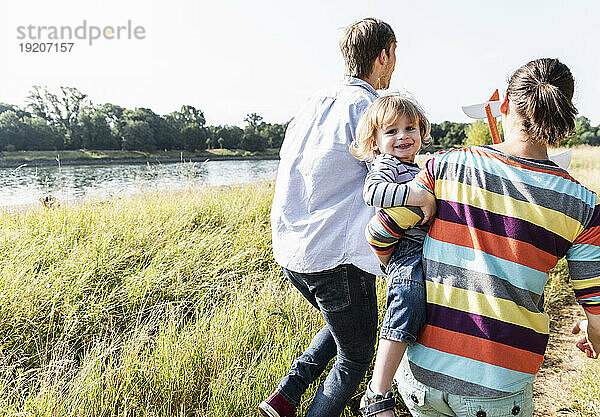 Glückliche Familie  die an einem schönen Sommertag am Flussufer spaziert