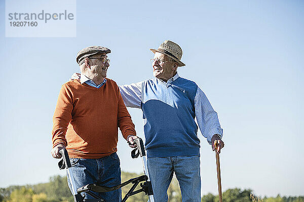 Alte Freunde spazieren mit Spazierstock und Rollator über die Felder und reden über alte Zeiten