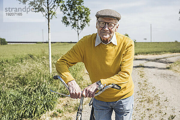 Lächelnder älterer Mann steht an einem sonnigen Tag mit dem Fahrrad