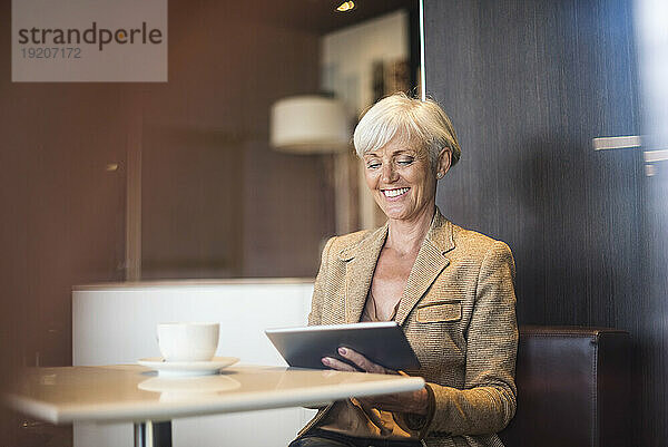 Lächelnde ältere Geschäftsfrau mit Tablet in einem Café