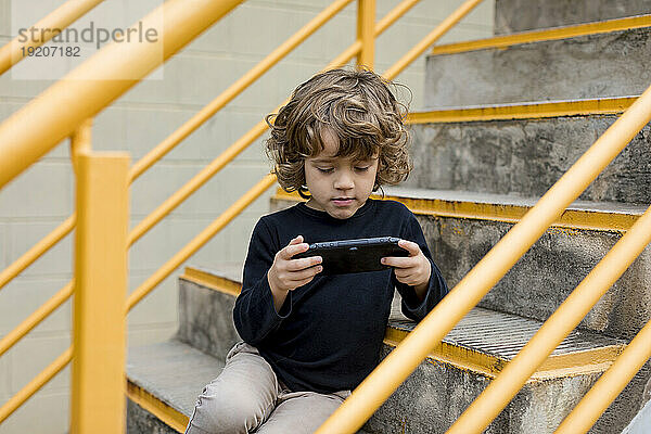 Boy sitting on stairs playing with handheld game console