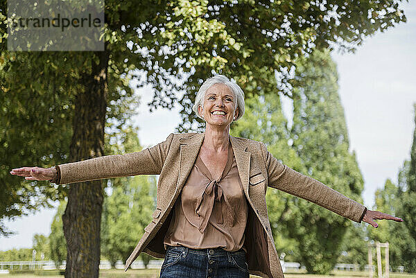 Glückliche ältere Frau mit ausgestreckten Armen in einem Park
