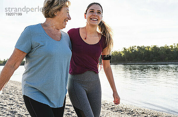 Fitte Großmutter und Enkelin gehen mit umschlungenen Armen am Fluss spazieren und haben Spaß