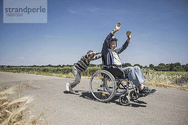 Junge schiebt Rollstuhl mit älterem Mann an sonnigem Tag