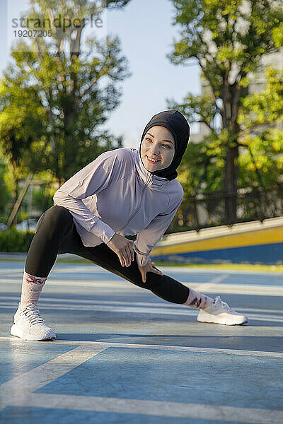 Lächelnde Frau  die sich auf dem Sportplatz dehnt