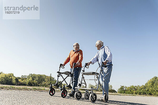 Two old friends walking on a country road  using wheeled walkers