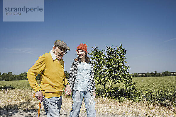 Glücklicher älterer Mann hält Händchen und geht mit Enkelin spazieren