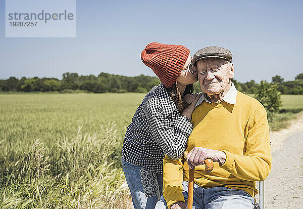 Mädchen mit Strickmütze küsst Großvater an sonnigem Tag