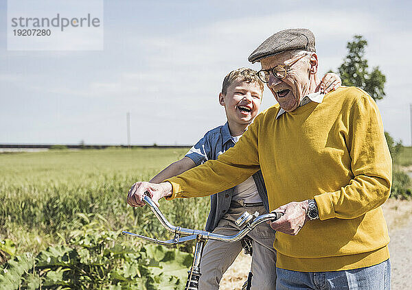 Fröhlicher älterer Mann mit Enkel sitzt auf dem Fahrrad