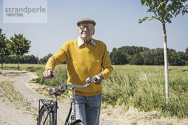 Lächelnder älterer Mann  der an einem sonnigen Tag mit dem Fahrrad läuft