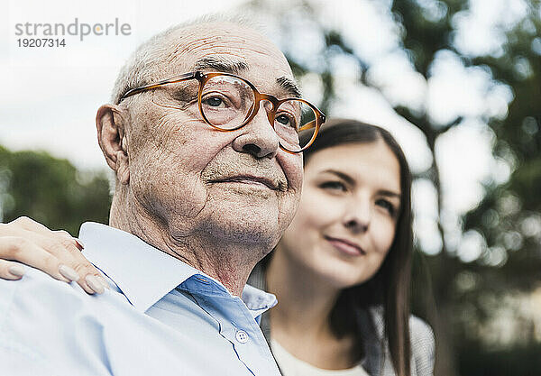 Portrait of self-confident senior man with granddaughter in the background