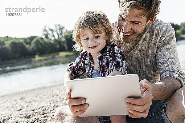 Vater und Sohn spielen am Flussufer auf einem digitalen Tablet
