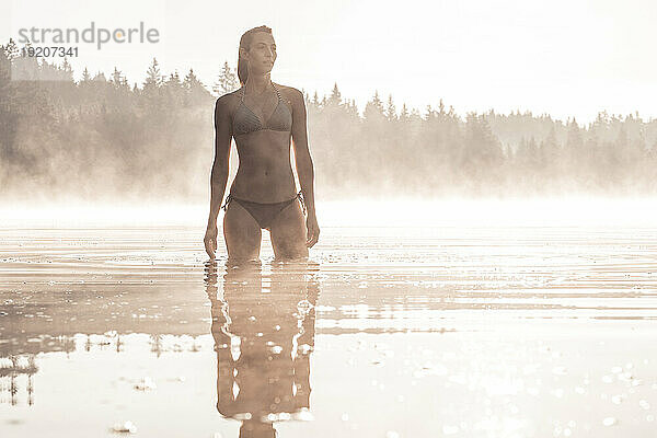 Frau im Bikini badet im Morgennebel in einem See